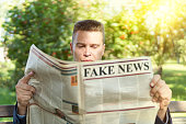 Close-up Of An Man Reading Fake News On Newspaper sitting on a bench in park