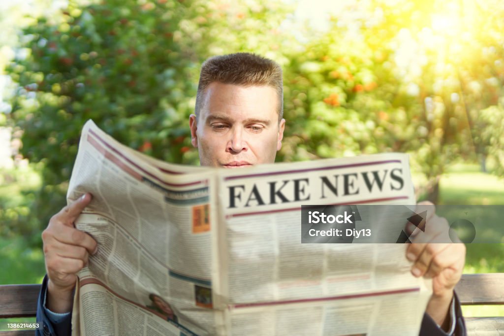 Close-up Of An Man Reading Fake News On Newspaper sitting on a bench in park Close-up Of An Man Reading Fake News On Newspaper sitting on a bench in the park Examining Stock Photo