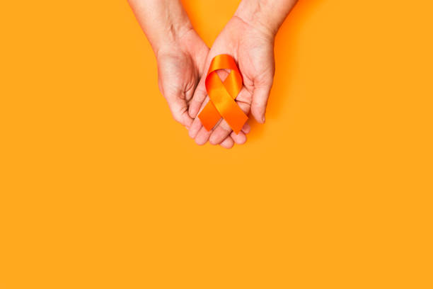 Woman hand holding a orange ribbon on a orange background Woman hand holding a orange ribbon on a orange background with copy space sclerosis stock pictures, royalty-free photos & images