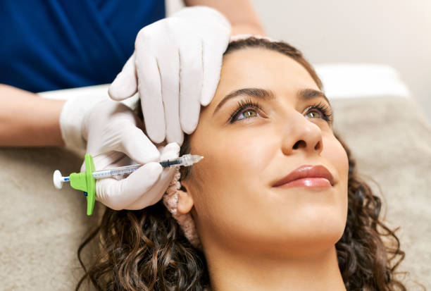 Cosmetologist making botox injection to client during skin care treatment Crop beautician in gloves doing filler injection in cheek zone to charming female client during rejuvenation procedure in cosmetology clinic cheek stock pictures, royalty-free photos & images