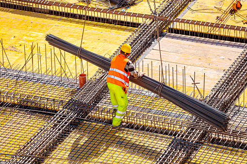 New delivery of construction steel to the construction site. A construction worker is stacking a batch of construction steel with a crane. Steel reinforcement, steel bars. Steel bars used in construction.