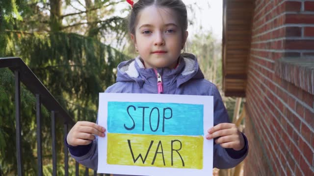 Ukrainian poor toddler girl kid homeless protesting armored conflict holding banner with inscription message text Stop War on background of yellow blue flag