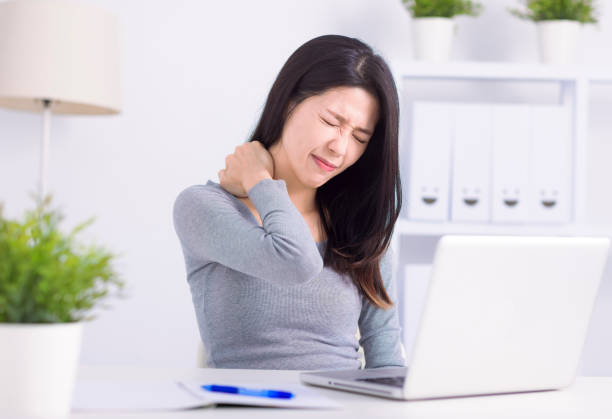 mujer joven sentada en el escritorio frente a la computadora portátil, toca el cuello siente dolor - pain shoulder human joint cramp fotografías e imágenes de stock