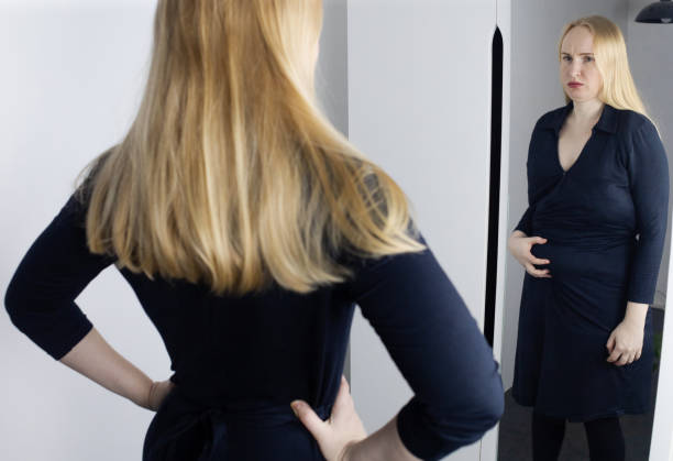 Eating disorder. Woman stands in front of the mirror and sees herself differently. Thin and fat female in frame. Dysmorphophobia or dysmorphia. BDD. Concept of psychological disorders and problems. stock photo