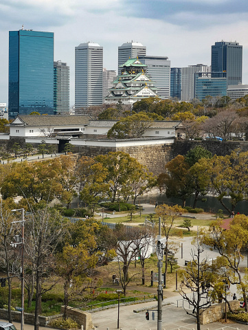Osaka, Japan - March 28, 2019: The iconic five storey tower of Osaka Castle surrounded by the leafy foliage of Osaka Castle Park and overlooked by the modern skyscrapers of downtown Osaka, Japan's vibrant second city. Panoramic image created from nine contemporaneous sequential photographs.