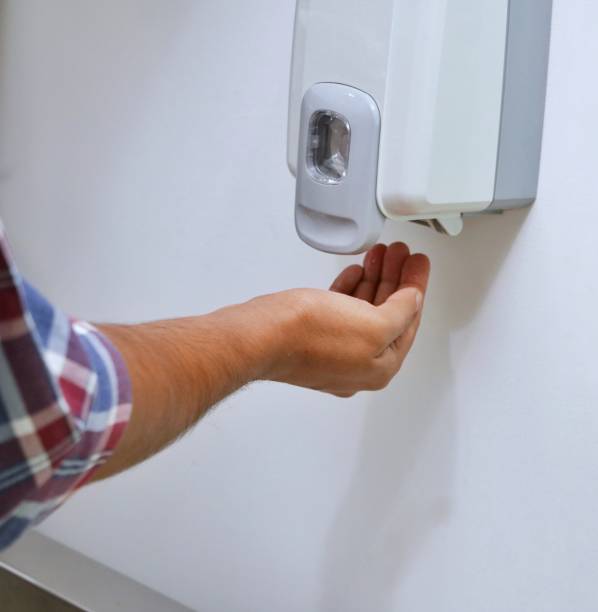 istock A man is kept hands under an automatic wall mounted sanitizer dispenser. 1386240244