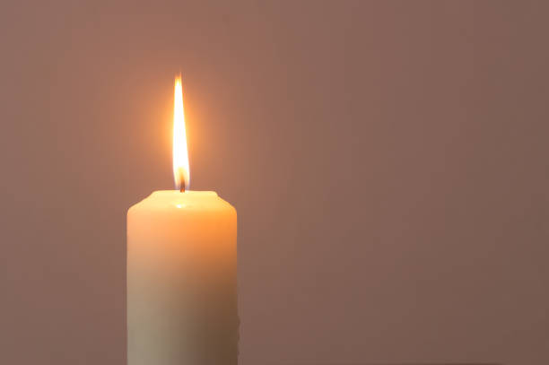 istock A single burning candle flame isolated on grey or dark background on table in church for Christmas, funeral and memorial service 1386241592