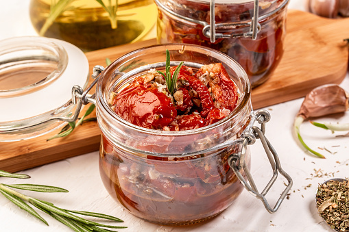 Food recipe background. Close up Sun dried tomatoes with garlic, oregano, olive oil in a jar on a light table, top view .