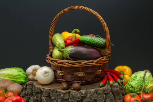 Fresh vegetables in a wicker basket on a stump with black background and copy space.
