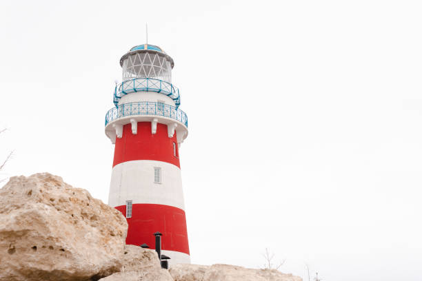 istock A red and white striped lighthouse during an early spring against clear white sky. Rocks, house and a road is on the bottom of the shot 1386251054