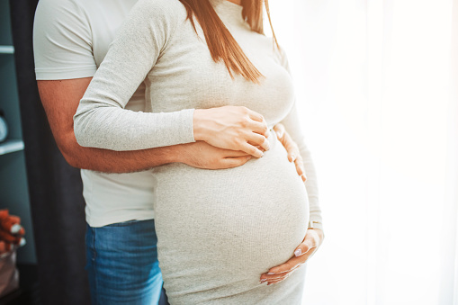 Pregnant woman and her man standing by the window