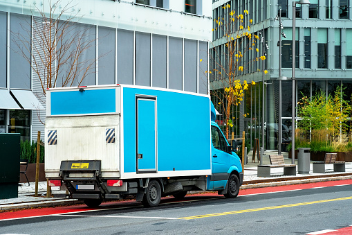 A blue commercial delivery van stands on a street in the city. Mock-up of the company logo