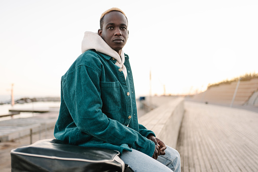 Focused black african man sitting on wooden wall thinking and looking to the side