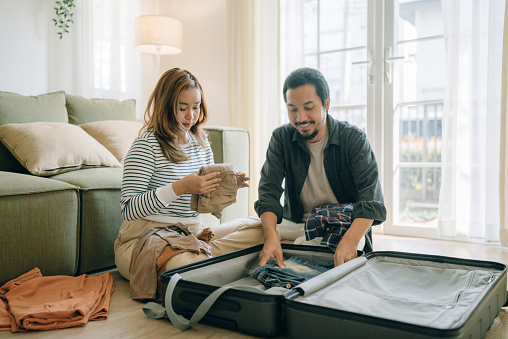 Asian couple travelers at home before road trip. They are putting cloths for summer vacation and prepare packaging of luggage. Travel suitcase close and ready to airport departure