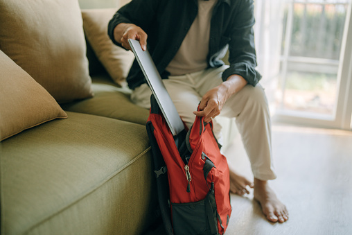 Close up of a young man packing his backpack (rucksack) in living room in preparation for going away.