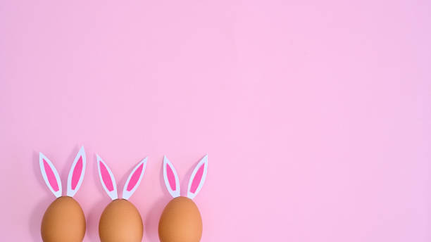 istock Three natural eggs with rabbit ears peek on pastel pink background with copy space. Easter flat lay minimal 1386276413
