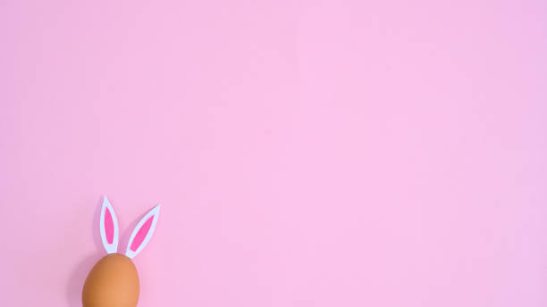 istock Natural egg with rabbit ears peek on pastel pink background with copy space. Easter flat lay minimal 1386276657