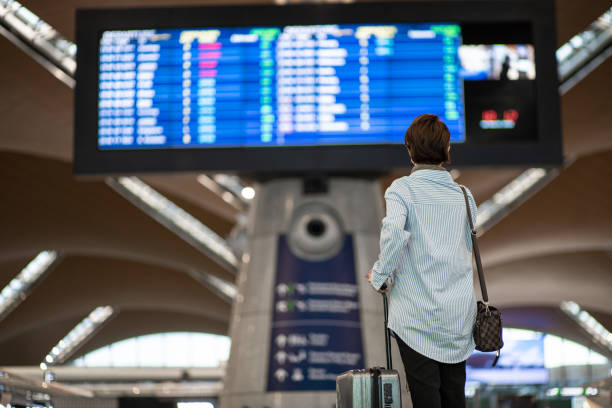 Rear view. Asian Chinese woman checking boarding time in airport.  Waiting in front arrival departure board. stock photo