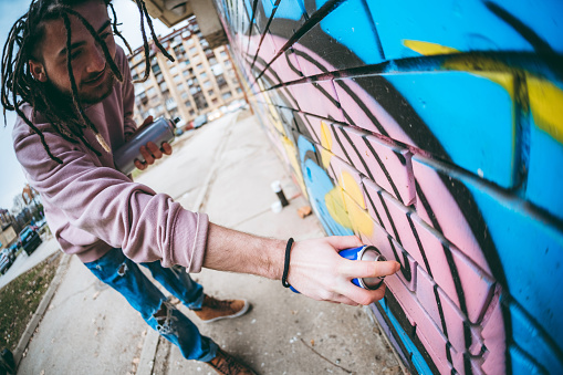 Young caucasian graffiti artist with dreadlocks painting graffiti.