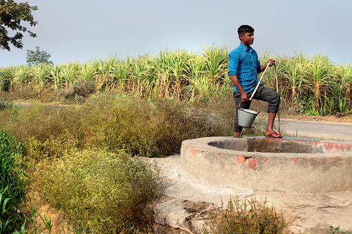 Rural farmer pulling water from water well near green field portrait outdoor in nature.