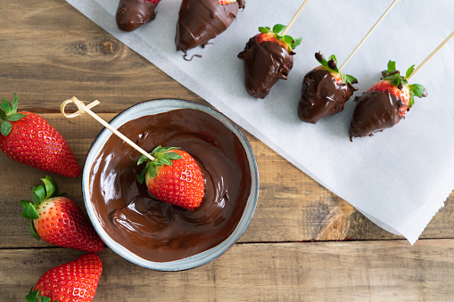 Strawberries with chocolate on a wooden background. Strawberries dipping process in chocolate. Copy space.