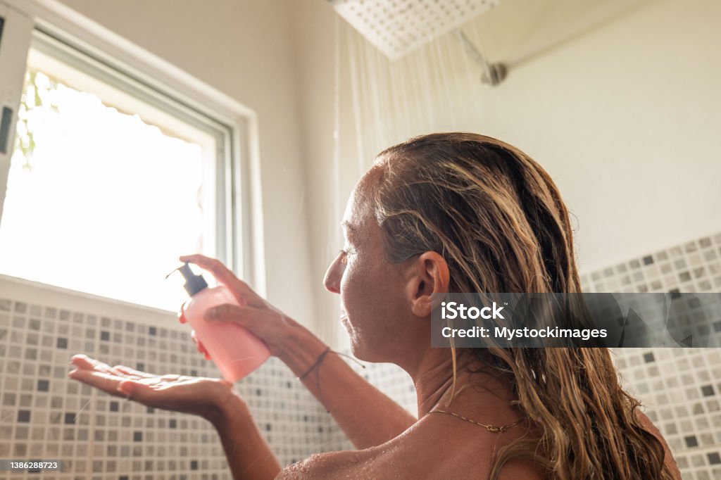 Woman takes shower and uses pink conditioner Low angle view, she enjoys the rain shower under the sunlight Hair Conditioner Stock Photo
