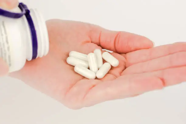 White capsule pills in a female hand close-up. Pills for unwanted pregnancy, oral contraception.