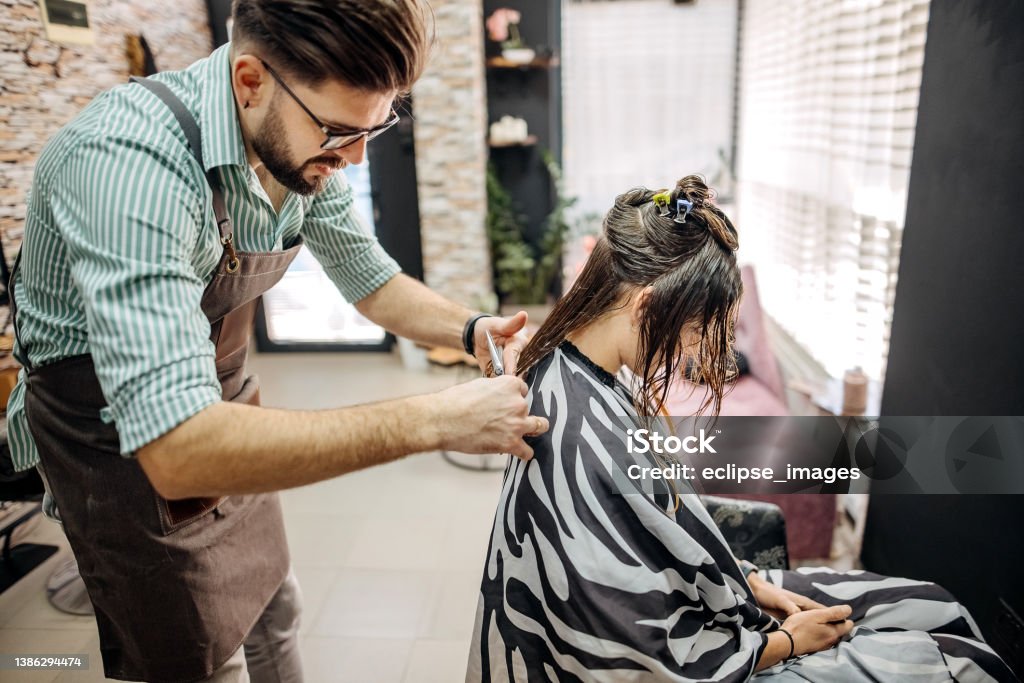 Let's straighten it out a bit Handsome male hairdresser styling and treating a woman's hair inside a salon Beautician Stock Photo