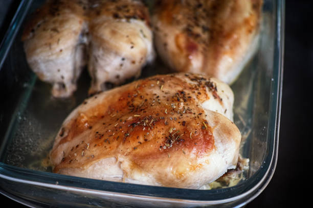 Roasted chicken breasts in a glass baking tray with spices on them. Close up.