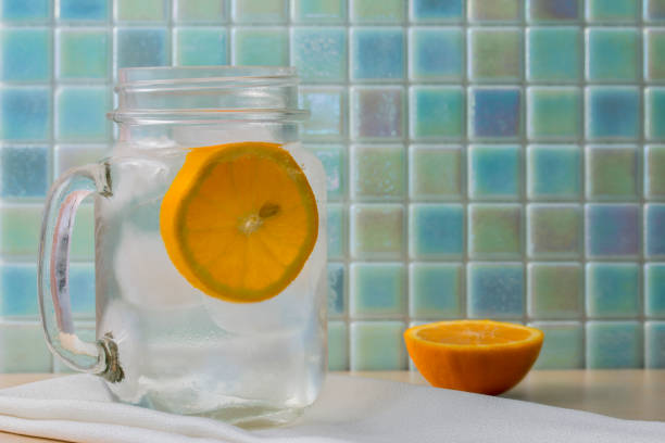 Ice water in a glass jar with orange slice on blue background stock photo