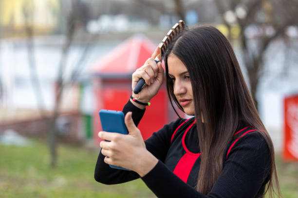 istock Beautiful girl combing using smart phone as a mirror in a park 1386332697
