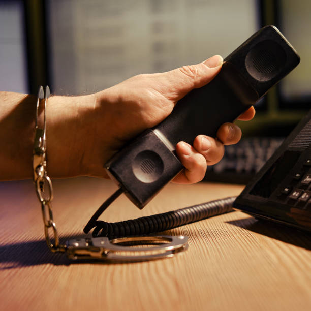 mężczyzna przy telefonie w kajdankach na rękach, z bliska. biurko biurowe w ciemnym pokoju nocnym z monitorami komputerowymi - freedom legal system handcuffs security zdjęcia i obrazy z banku zdjęć