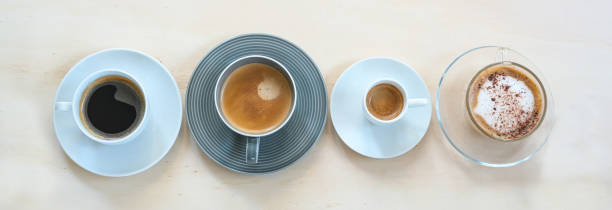 istock Four cups with various coffee, espresso, cappuccino, lungo, black and with crema on a light wooden table, panoramic format, copy space, high angle view from above 1386334690