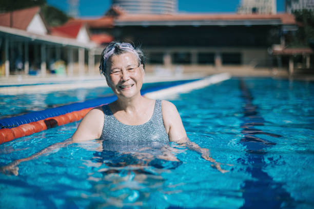 asiatische chinesische seniorin, die am wochenendmorgen lächelnd in die kamera im schwimmbad schaut - active seniors retirement enjoyment swimming pool stock-fotos und bilder