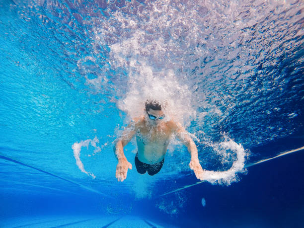 vue sous-marine en contre-plongée nageur asiatique chinois nageant avec style papillon dans la piscine - swimming trunks men muscular build athlete photos et images de collection