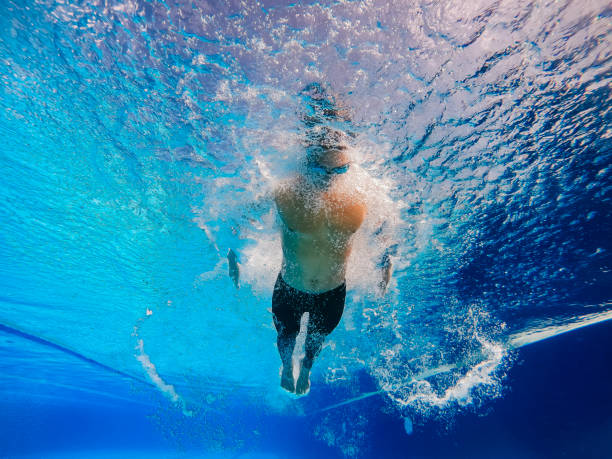 vue sous-marine en contre-plongée nageur asiatique chinois nageant avec style papillon dans la piscine - swimming trunks men muscular build athlete photos et images de collection