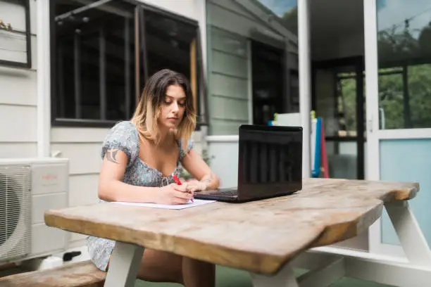 The shot of young Maori woman working from home using internet and writing on paper.