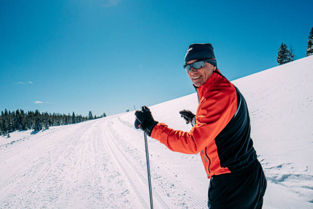 close-up medium portrait of a cheerful cross-country skier looking back at camera while skiing along a groomed trail on a clear, sunny day in the grand mesa national forest in colorado with copy space - nordic event fotos imagens e fotografias de stock