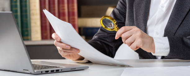 manos femeninas con una lupa dorada y un papel en el escritorio junto a la computadora portátil abierta, de cerca, enfoque seleccionado. - fine print fotografías e imágenes de stock