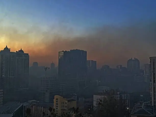 Kyiv city capital of Ukraine in acrid smoke after the explosion in the early morning time, view through the glass of the window. The lights were turned off in the houses due to the curfew.