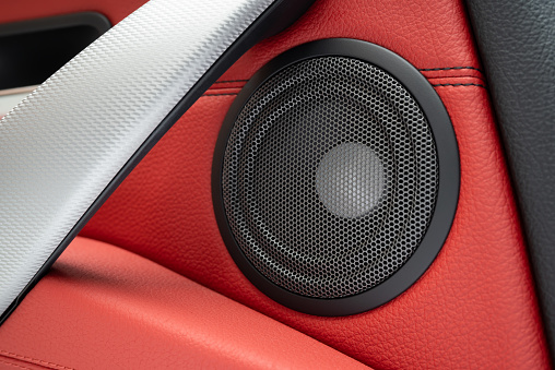 Close up of premium car speaker on a red leather door panel.