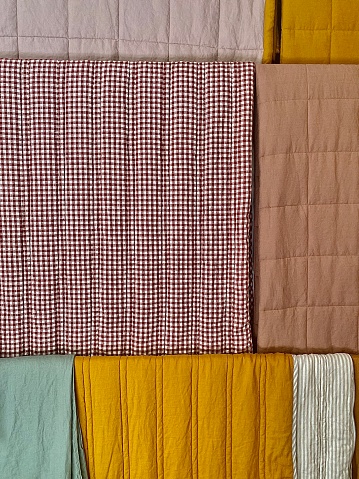 Vertical close up of variety of material fabric bedding materials in color and checkers hanging up