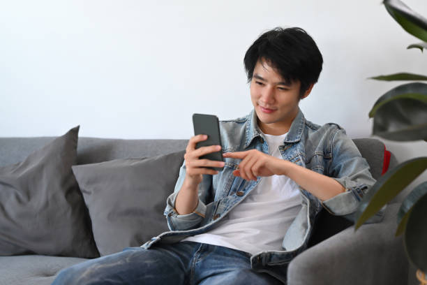 istock Happy man in casual wear using smart phone, checking social media, ordering delivery while relax on sofa. 1386392996