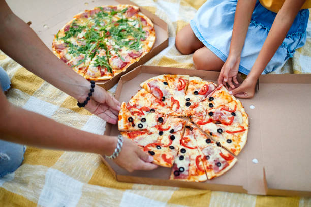 istock Sharing pizza, hands taking a piece of pizza from a box outdoor, 1386398324