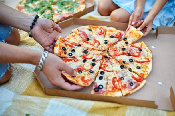 istock Sharing pizza, hands taking a piece of pizza from a box outdoor, 1386398325
