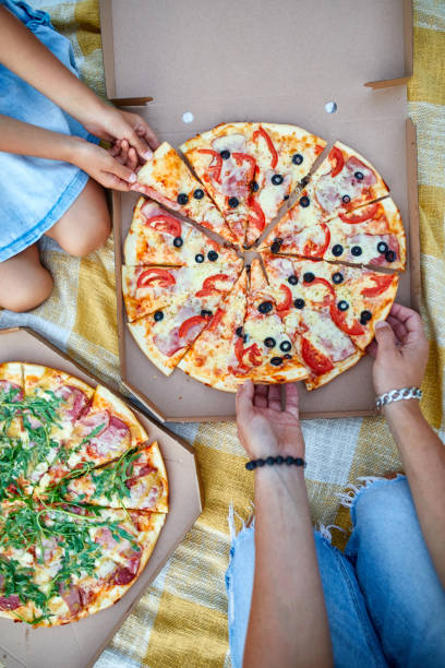 istock Sharing pizza, hands taking a piece of pizza from a box outdoor, 1386398326