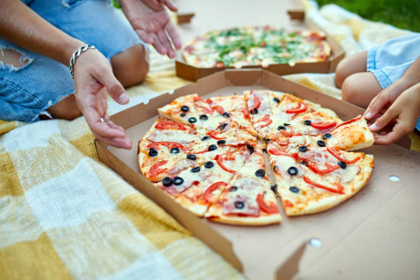 istock Sharing pizza, hands taking a piece of pizza from a box outdoor, 1386398327