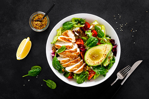 Grilled chicken breast and fresh vegetable salad of tomato, avocado, lettuce and spinach. Top view, flat lay