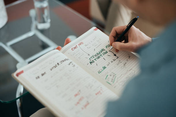 Close-up of patient brainstorming in notebook during counseling with mental health professional. Close-up of man brainstorming and writing notes during therapy session with his psychiatrist. personality test stock pictures, royalty-free photos & images