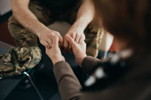 close-up de psicoterapeuta de mãos dadas com um soldado durante o aconselhamento em seu escritório. - veteran - fotografias e filmes do acervo